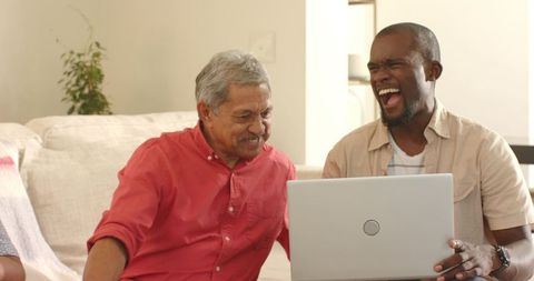 Multigenerational Friends Laughing Over Laptop in Cozy Living Room, Senior and African American Men