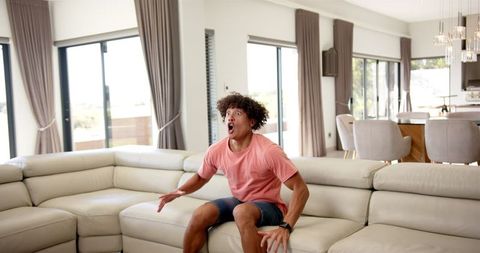 Excited man jumping on couch in modern living room