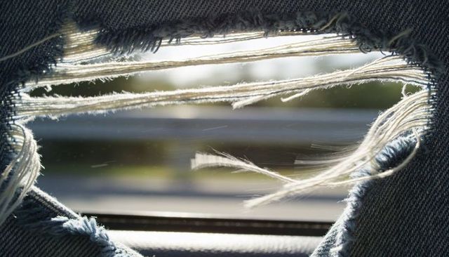 Ripped blue denim framing highway view with frayed white threads through car window
