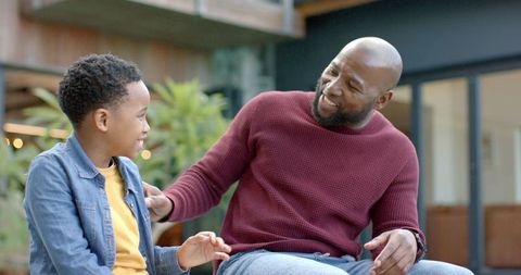 African american father sharing joyful smiling moment with son on outdoor bench casual