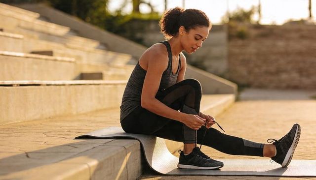 Tying running shoes on exercise mat on concrete steps during golden hour outdoor workout