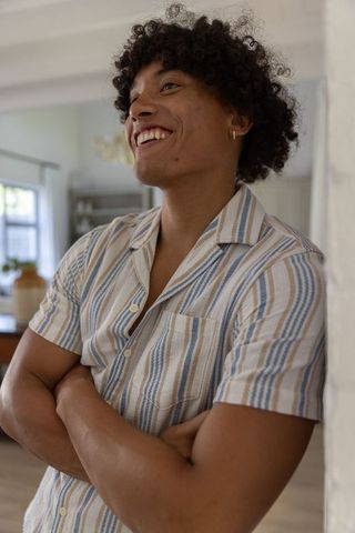 Smiling young man leaning against wall in sunlit open-plan kitchen, casual striped shirt