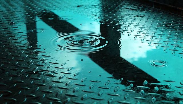 Walking silhouette reflecting on wet diamond plate with raindrop ripples and urban steel