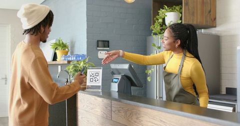 African american barista accepting mobile qr payment at modern cafe counter, smiling