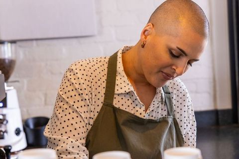 Shaved head female barista preparing espresso behind counter in minimalist coffee shop
