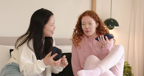Friends sharing smartphone moments on couch in cozy hoodies laughing together