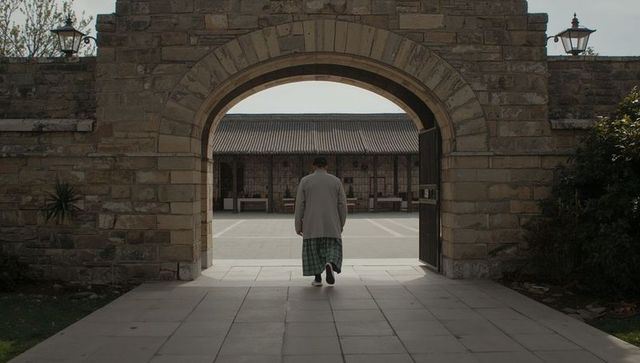Solitary man walking through historic stone arch toward tranquil sunlit courtyard