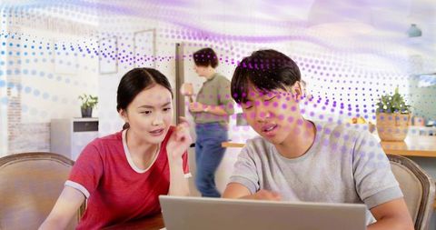 Young couple collaborating on laptop at kitchen table with purple dotted digital overlay