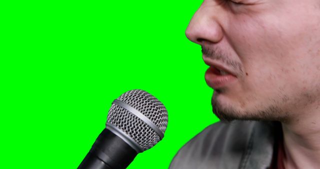Close-up of man singing into a microphone in front of a green screen background. Perfect for music studio ads, vocal recording sessions, and performance tutorials.