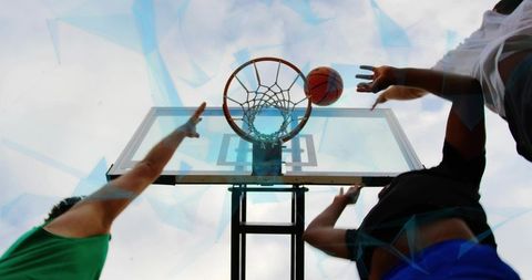 Low-angle action of leaping players reaching for basketball rim during outdoor street game