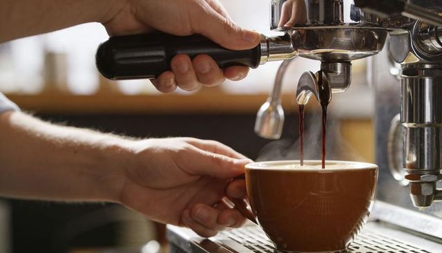 Barista pulling espresso shot over ceramic cup from chrome machine with visible crema
