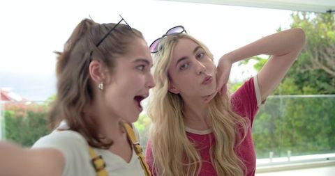 Young women posing for selfie on glass balcony with sunglasses and relaxed summer vibe