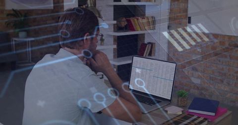 Mid-adult man working on laptop with data overlay and circuitry in modern loft workspace