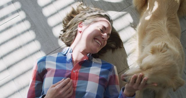 Caucasian woman smiling and lying on floor with dog. domestic life, spending free time relaxing at home.