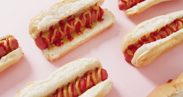 Appealing image showing hot dog sandwiches with mustard and ketchup on a pink background. Ideal for use in food-related blogs, advertisements for fast food or summer-themed events, menu designs, street food promotions, and culinary articles.