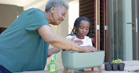 African grandmother teaching granddaughter gardening on patio with raised planter