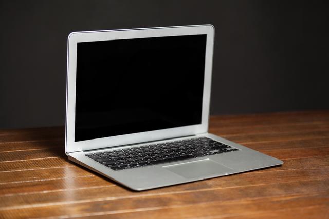 This image shows an open laptop placed on a wooden table with a dark background. It is ideal for use in articles or advertisements related to technology, remote work, modern office setups, and digital devices. It can also be used in blogs or websites focusing on business, productivity, or electronics.