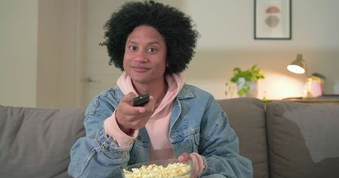 Mid-adult man on couch holding remote and popcorn enjoying cozy movie night at home