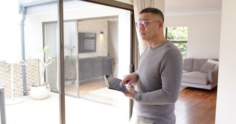 Senior man using tablet by glass door in modern living room