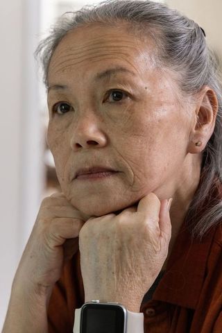 Senior asian woman resting chin on fists wearing smartwatch, contemplative elderly portrait serene