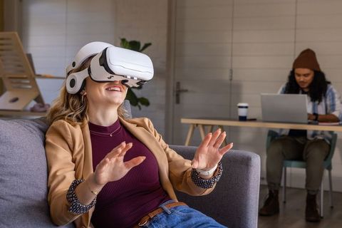 Woman Wearing VR Headset Enjoying Virtual Reality While Coworker Working in Modern Lounge