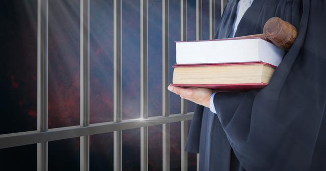 Judge holding books and a gavel in front of prison cell bars. This image can be used for articles, websites, or presentations related to law, justice system, criminal law, court proceedings, or prison reform.