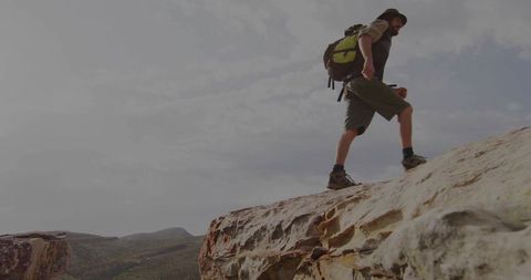 Hiker climbing sandstone mesa edge wearing wide-brim hat and green backpack on cliff