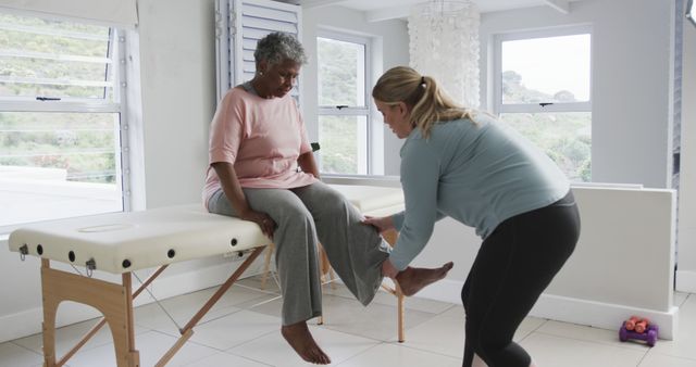 An elderly woman undergoes a physical therapy session at a health clinic. A healthcare professional assists her by working on her leg muscles. This could be used in articles or websites related to elderly care, rehabilitation, physical therapy, and healthcare services.