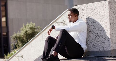 Contemplative African American Man on City Steps with Smartwatch and Casual Streetwear