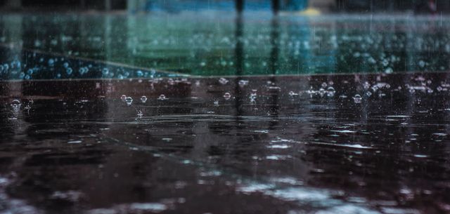 This image captures raindrops splashing on a wet, reflective surface, perfect for use in projects about weather, rainy days, or the natural beauty of water in motion. Useful for web design, blogs, social media posts, or any material discussing weather patterns, moods, or environmental conditions.