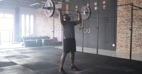 Dedicated man performing overhead barbell lift at modern gym
