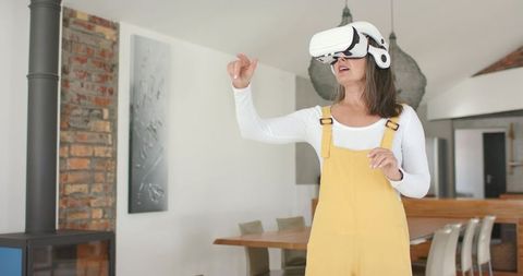 Senior woman exploring virtual reality at home wearing vr headset and yellow overalls