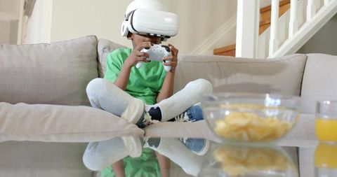Young boy playing virtual reality game on couch with snacks and controller