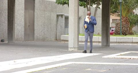 Professional African American Man Walking Through Urban Plaza Holding Coffee and Snack