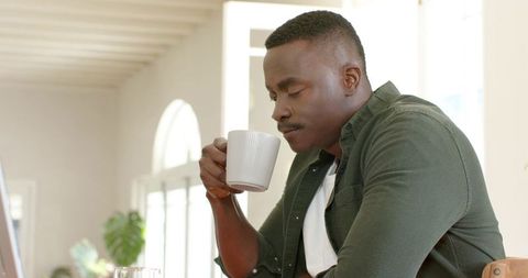 African american man sipping coffee at dining table in sunlit home, relaxed morning routine