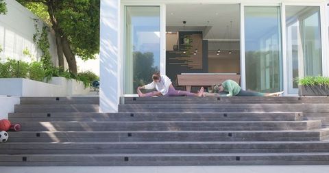 Two women stretching on tiered patio steps at home during outdoor morning fitness routine