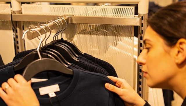 Female shopper examining navy sweater on metal rack in warm retail lighting