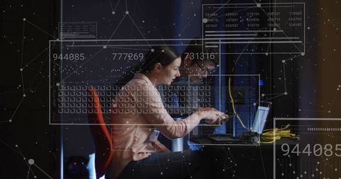 Female it specialist pointing at laptop while colleague troubleshooting servers with hud overlay