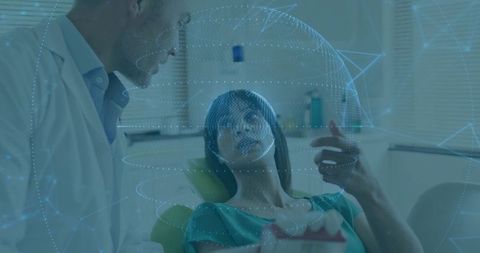 Dentist consulting patient with holographic dental overlay while holding jaw model