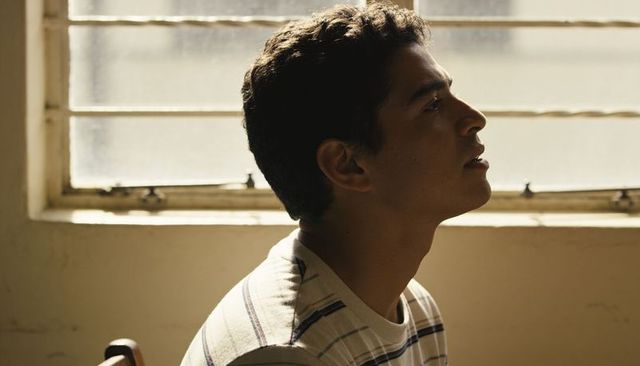 Young man gazing upward in warm backlight by frosted window, contemplative profile portrait