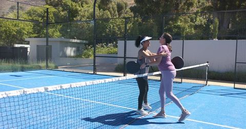 Two women embracing and greeting over net on blue padel court wearing activewear