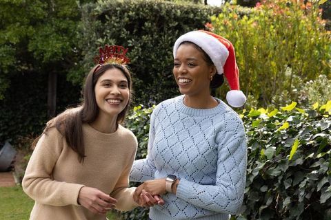Diverse women celebrating christmas in backyard wearing santa hat and merry headband