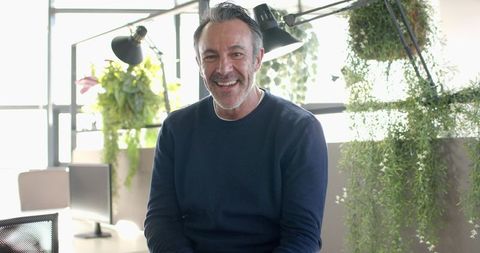 Mature professional smiling while sitting at bright biophilic office desk with greenery