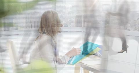 Businesswoman holding teal folders at desk with blurred pedestrians and city skyline