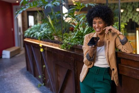 African american businesswoman laughing in modern office lounge with smartphone