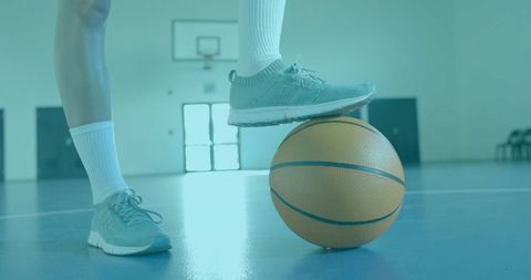 Female athlete pressing foot on basketball on indoor court balancing ready to dribble