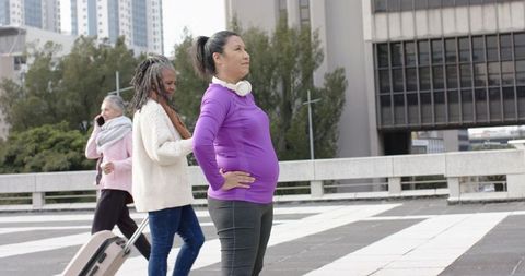 Diverse women walking urban plaza, confident woman with headphones and hands on hips