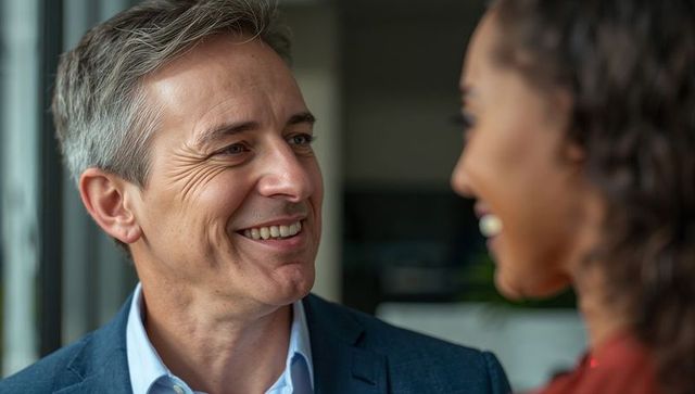 Middle-aged businessman smiling while talking with colleague by office window, professional