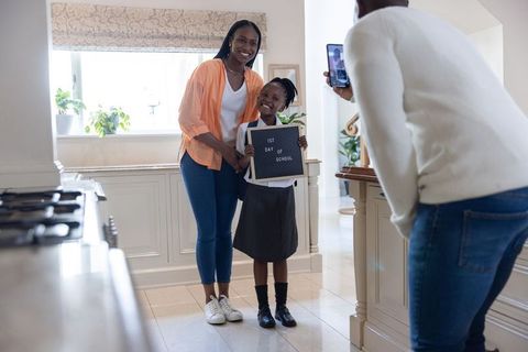 African american mom and daughter holding 1st day of school sign while dad using phone