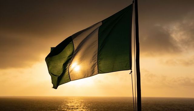 Fluttering nigerian flag backlit by golden sunset over ocean, silhouette mast and halyard